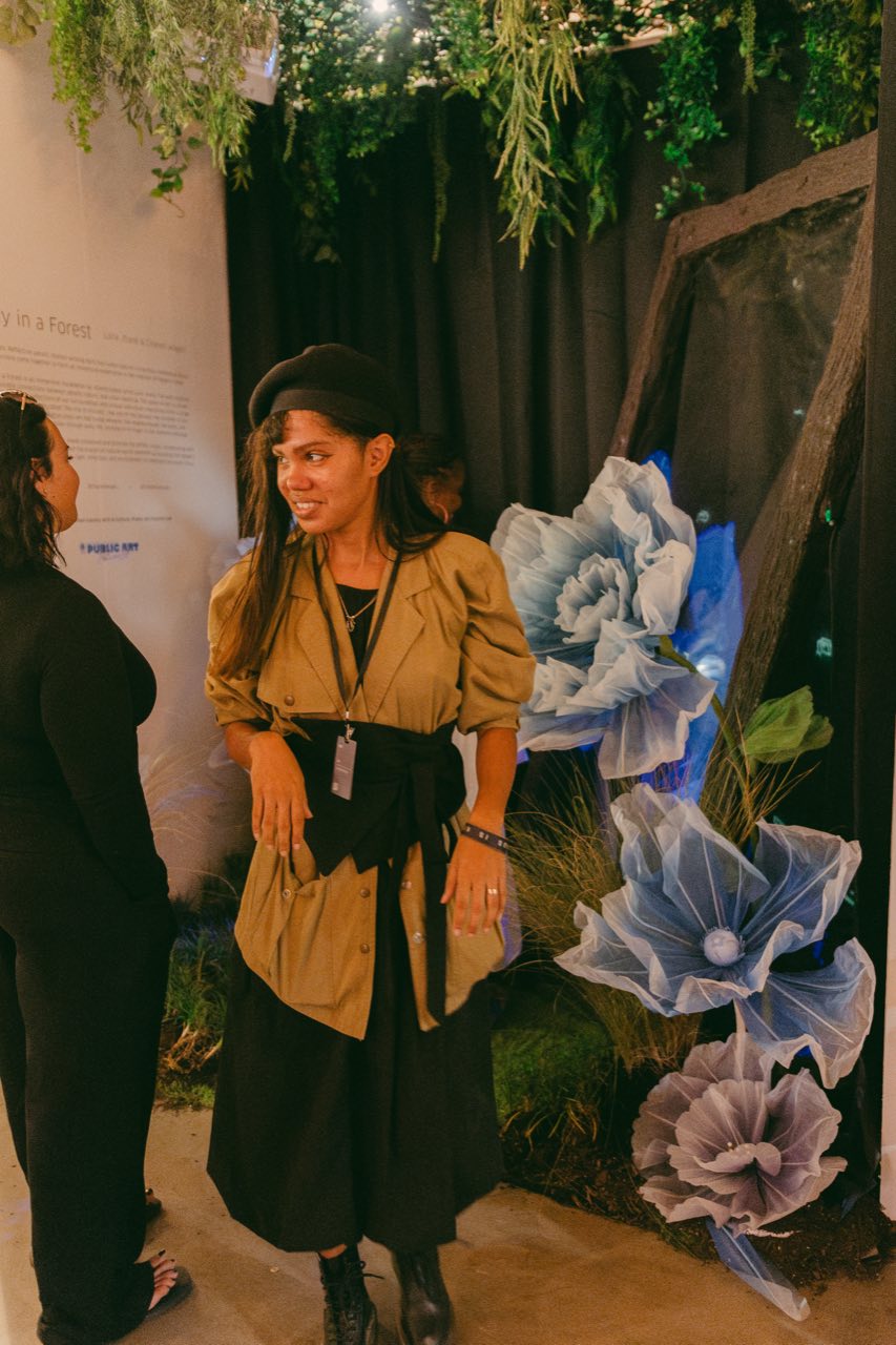 A visitor posing among the giant blue and violet blooms beside the exhibition text panel.